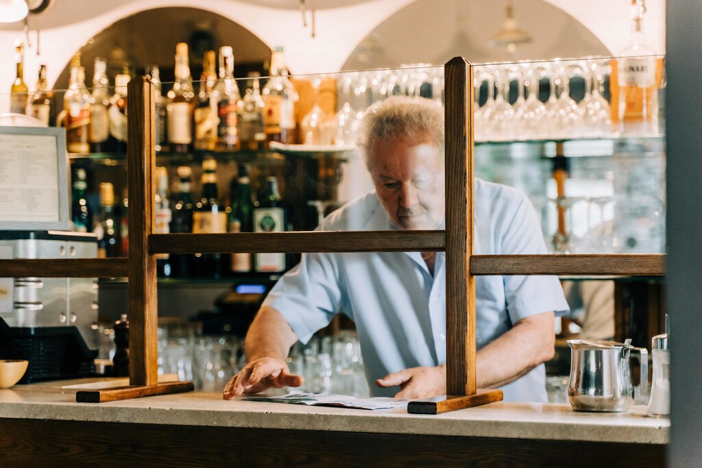 Bartender serving customers from behind a protective screen erected by law to guard him against COVID-19 in a bar