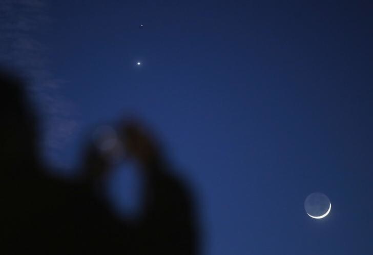A man takes a picture of the crescent moon and planets Venus and Mars seen in the sky in central Bosnia February 20, 2015. People in Bosnia witnessed late Friday evening an astronomical event whereby Venus and Mars were accompanied by a crescent moon just after sunset. REUTERS/Dado Ruvic (BOSNIA AND HERZEGOVINA - Tags: ENVIRONMENT)