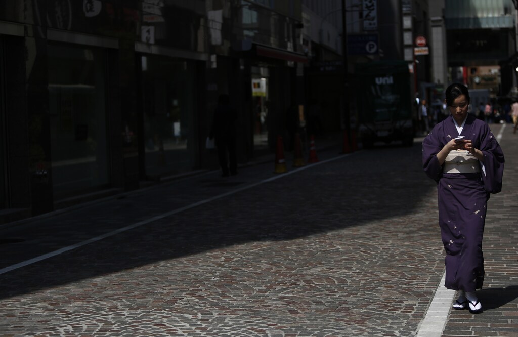 A woman using her mobile phone walks on a street at Ginza shopping district in Tokyo April 25, 2014. Tokyo's inflation jumped to a 22-year high in April by a key measure, an early sign that companies are making progress in passing on a new tax increase to customers as policy makers seek to pull Japan out of years of deflation. REUTERS/Yuya Shino (JAPAN - Tags: POLITICS BUSINESS) - GM1EA4P13QD01