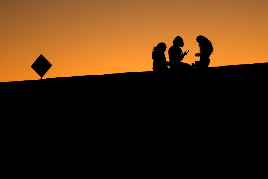 Young girls look at their phones as they sit on a hillside after sun set in El Paso, Texas, U.S., June 20, 2018. REUTERS/Mike Blake - RC182A561FE0