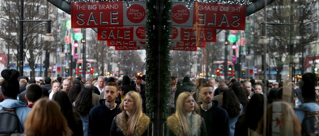 Shoppers are reflected in a store window as they pass sales advertisements on Oxford Street in London, Britain December 26, 2015.