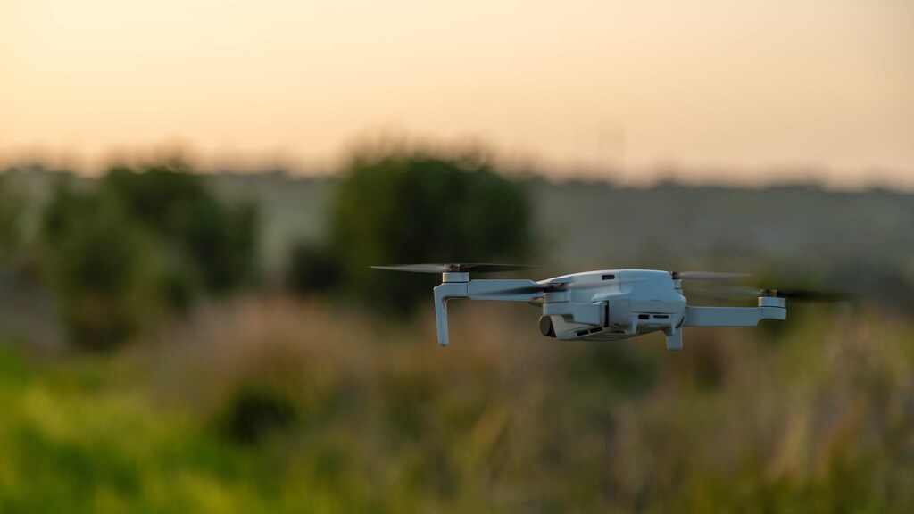 A drone hovering over the ground in a field during sunset.