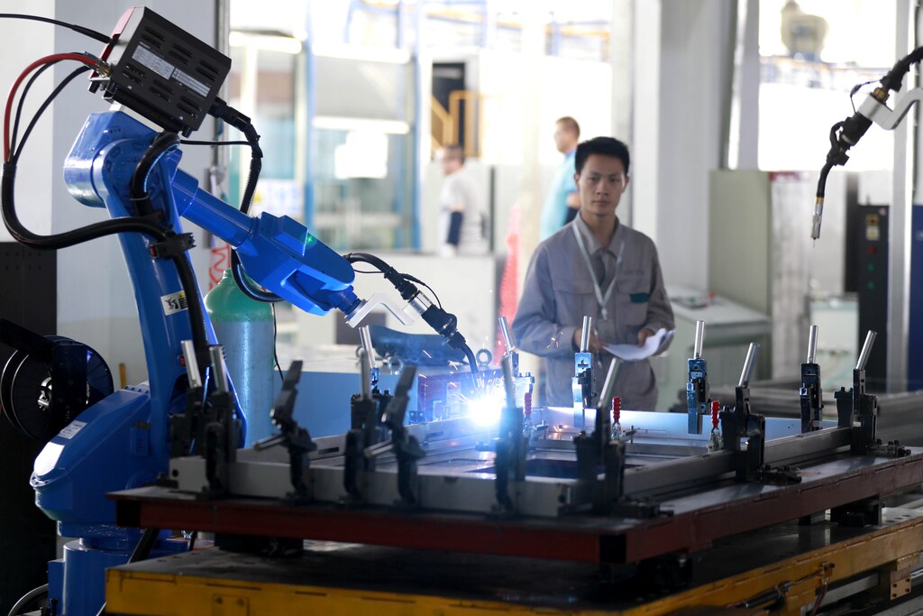 A worker monitors a robotic arm working inside a factory in Huaian, Jiangsu province, China May 15, 2018. Picture taken May 15, 2018. REUTERS/Stringer ATTENTION EDITORS - THIS IMAGE WAS PROVIDED BY A THIRD PARTY. CHINA OUT. - RC1360033A90