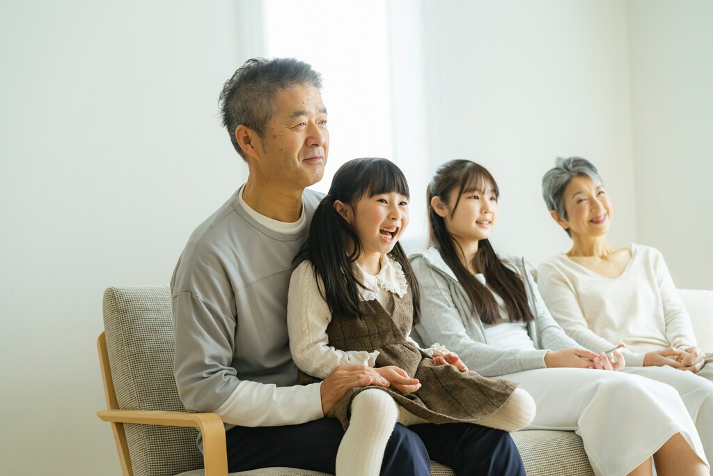 A family of four - two grandparents and two grandchildren - sit on a sofa together smiling.
