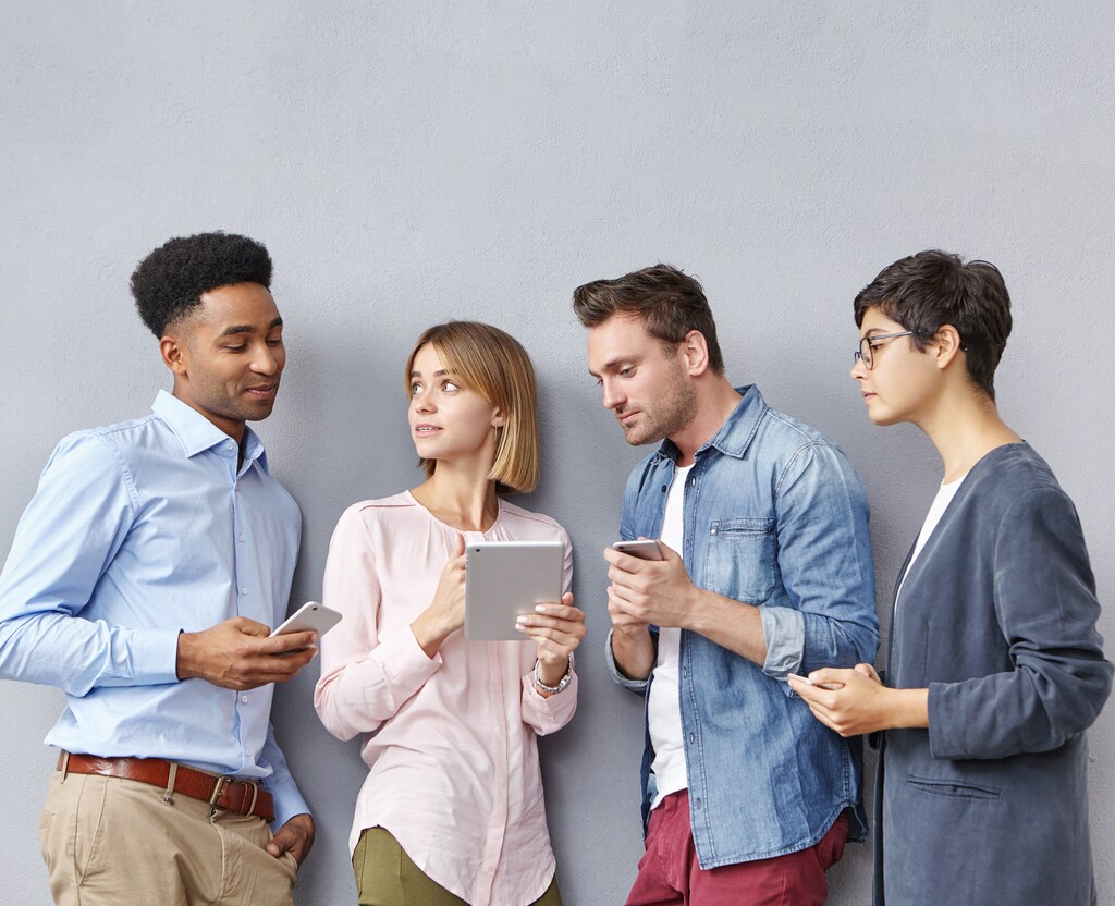 Modern education, business, startup, friendship and teamwork concept. International team of diverse ambitious talented young people standing in line in studio, using electronic gadgets and talking