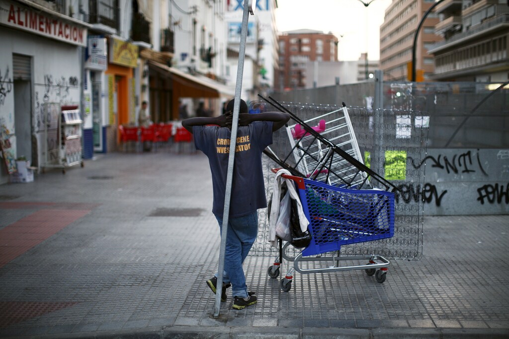A scrap dealer leans on a traffic signal and watches as protesters (not pictured) take part in a "March for dignity" to protest against austerity measures under the slogan "Pan, techo, trabajo y dignidad" (Bread, housing, job and dignity) in downtown Malaga, southern Spain, October 22, 2015. Spain's unemployment rate has fallen to its lowest level in over four years and is now lower than when Prime Minister Mariano Rajoy took office, potentially boosting his chances in an election less than two months away. Frustration over an enduring jobs crisis will weigh on the Dec. 20 vote, with many Spaniards divided over whether their prospects are improving after a double-dip recession that sent unemployment soaring to nearly 27 percent in 2013. REUTERS/Jon Nazca - GF20000028827