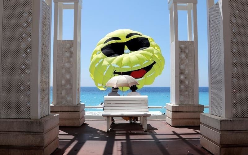 Two elderly people sit on a bench as they look at a happy face design on a parascending during a sunny day in Nice, France, June 1, 2018.