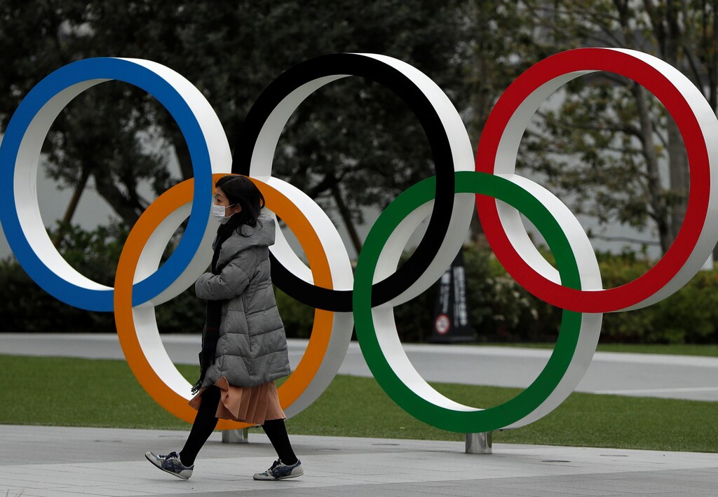 A woman wearing a protective face mask, following an outbreak of the coronavirus disease (COVID-19), walks past the Olympic rings in front of the Japan Olympics Museum, in Tokyo, Japan March 30, 2020. REUTERS/Issei Kato - RC24UF9610O6