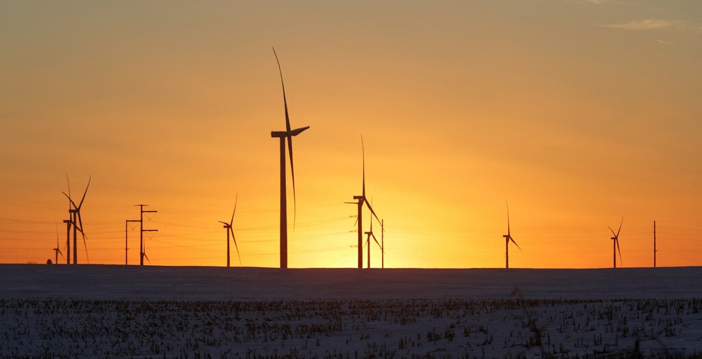 A wind farm against an orange sky. Our energy system is changing rapidly, and it is likely that 2024 will be our peak energy emissions.