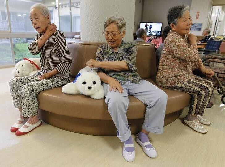 Ayako Shizo (C), aged 85, taps a therapeutic robot named Paro as she sits with other residents at the Suisyoen retirement home about 30 km (19 miles) south of the tsunami-crippled nuclear plant in Iwaki, Fukushima prefecture, July 28, 2011. For some elderly survivors of Japan's March earthquake and tsunami, comfort comes in the form of a small white robotic seal named Paro. The residents of the nursing home came back from a nearly two-month-long evacuation since the nuclear crisis in Fukushima. Picture taken July 28, 2011. To match Reuters Life! ROBOT-SEAL/ REUTERS/Kim Kyung-Hoon (JAPAN - Tags: SOCIETY SCI TECH IMAGES OF THE DAY)