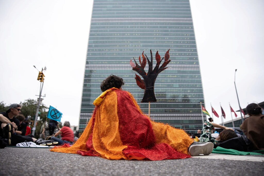 A protester holding a cardboard cut out of a tree on fire sits blocking the street in front of the United Nations during a 'non-violent resistance' climate change protest organized by Extinction Rebellion, where speakers demanded global leaders take more action before COP 26, in the Manhattan borough of New York City, U.S., September 17, 2021.
