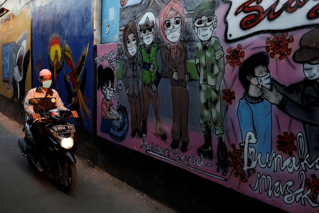 A man wearing a protective mask rides a motorbike past murals promoting awareness of the coronavirus disease (COVID-19), at an alley of a village in Bekasi, on the outskirts of Jakarta, Indonesia, July 28, 2020. REUTERS/Willy Kurniawan - RC2D2I9274IJ