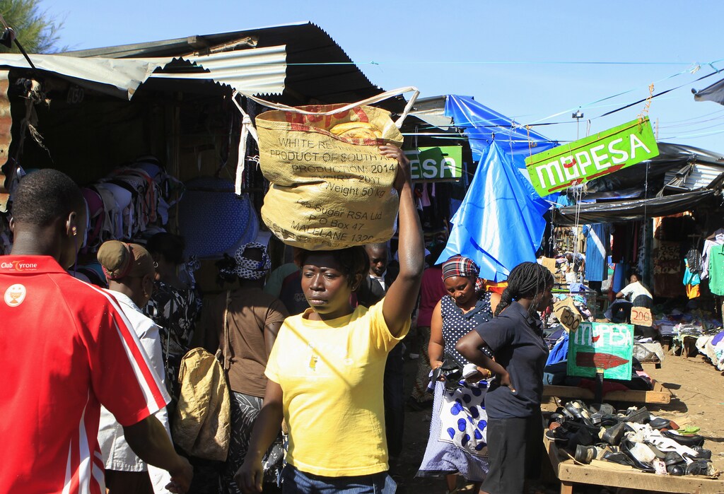 Kibera residents walk past an M-Pesa banner at an open-air market in Kenya's capital Nairobi December 31, 2014. Safaricom, Kenya's biggest telecoms firm, is a model of how technology can be used to financially include millions of people with mobile telephones but without access to traditional infrastructure such as the banks that are available to the wealthy or those living in cities. Safaricom in 2007 pioneered its M-Pesa mobile money transfer technology, now used across Africa, Asia and Europe. It proved that money can be made from people who earn a few dollars a day. REUTERS/Noor Khamis (KENYA - Tags: BUSINESS SOCIETY SCIENCE TECHNOLOGY TELECOMS) - RTR4JQ1G