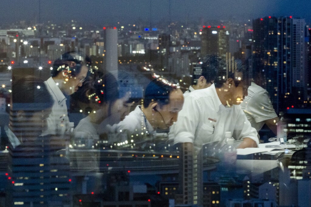 Reporters are reflected in a window overlooking Tokyo at night as they work at the Toshiba headquarters after a news conference July 21, 2015. Toshiba Corp's chief executive stepped down on Tuesday after an independent investigation found he had been aware the company had inflated its profits, in the country's biggest corporate scandal in years. REUTERS/Thomas Peter TPX IMAGES OF THE DAY - GF10000165717