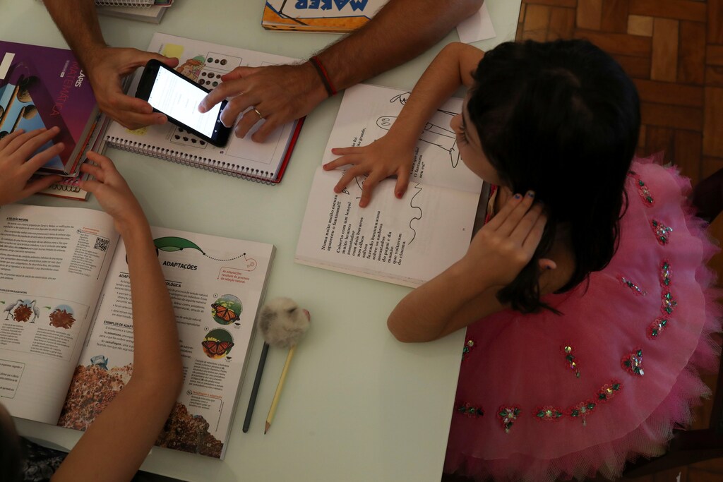 Alice, 5, watches a video sent by school as she studies at home with her father during a lockdown in Santo Andre, Brazil.