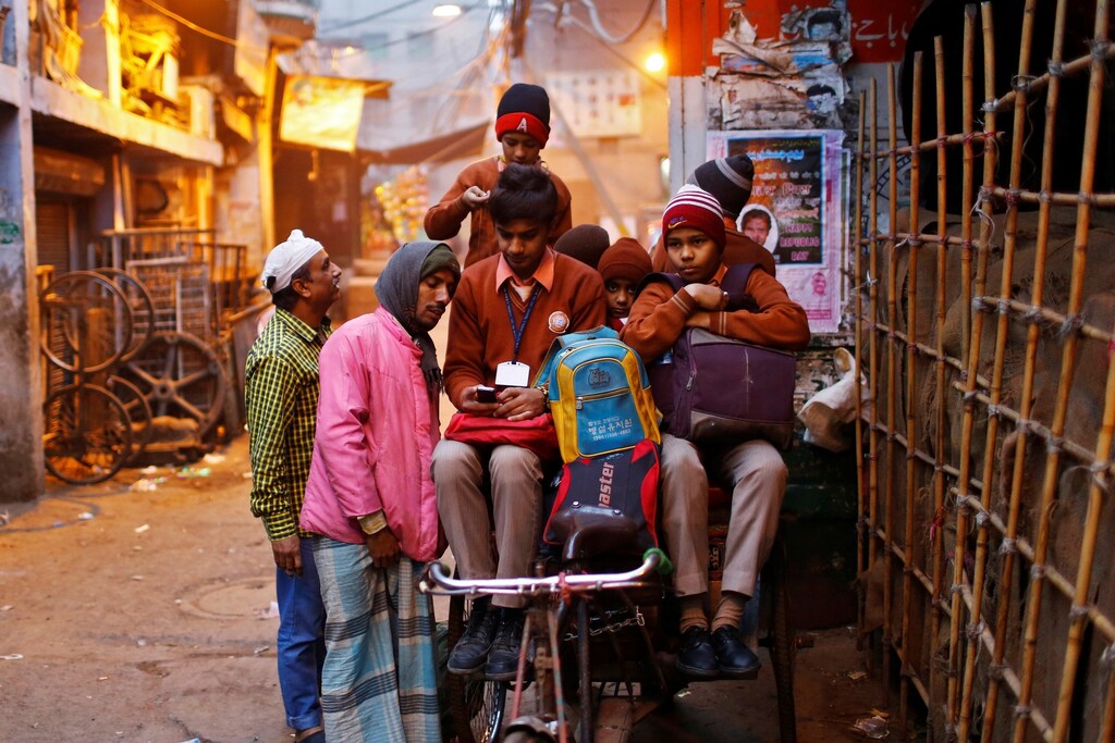 A schoolboy shows his mobile phone to a rickshaw puller takign him and other students to school on a cold winter morning in the old quarters of Delhi January 30, 2014.