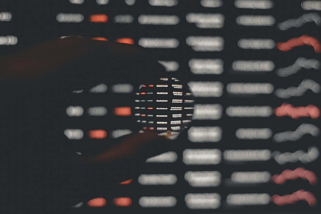 A hand holding a lens that zooms into a digital screen, black, white and orange: AI-first enterprises redesign processes around human-AI collaboration