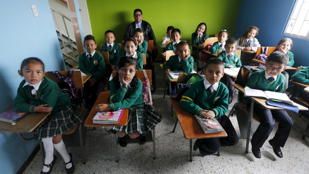Teacher Father Juan Humberto Cruz poses for pictures with 4th grade students at Semillas de Esperanza (Seeds of Hope) school in Soacha, near Bogota, Colombia, June 11, 2015. Nearly three years after Taliban gunmen shot Pakistani schoolgirl Malala Yousafzai, the teenage activist last week urged world leaders gathered in New York to help millions more children go to school. World Teachers' Day falls on 5 October, a Unesco initiative highlighting the work of educators struggling to teach children amid intimidation in Pakistan, conflict in Syria or poverty in Vietnam. Even so, there have been some improvements: the number of children not attending primary school has plummeted to an estimated 57 million worldwide in 2015, the U.N. says, down from 100 million 15 years ago. Reuters photographers have documented learning around the world, from well-resourced schools to pupils crammed into corridors in the Philippines, on boats in Brazil or in crowded classrooms in Burundi. REUTERS/John Vizcaino PICTURE 9 OF 47 FOR WIDER IMAGE STORY "SCHOOLS AROUND THE WORLD"SEARCH "EDUCATORS SCHOOLS" FOR ALL IMAGES - RTS2DUY