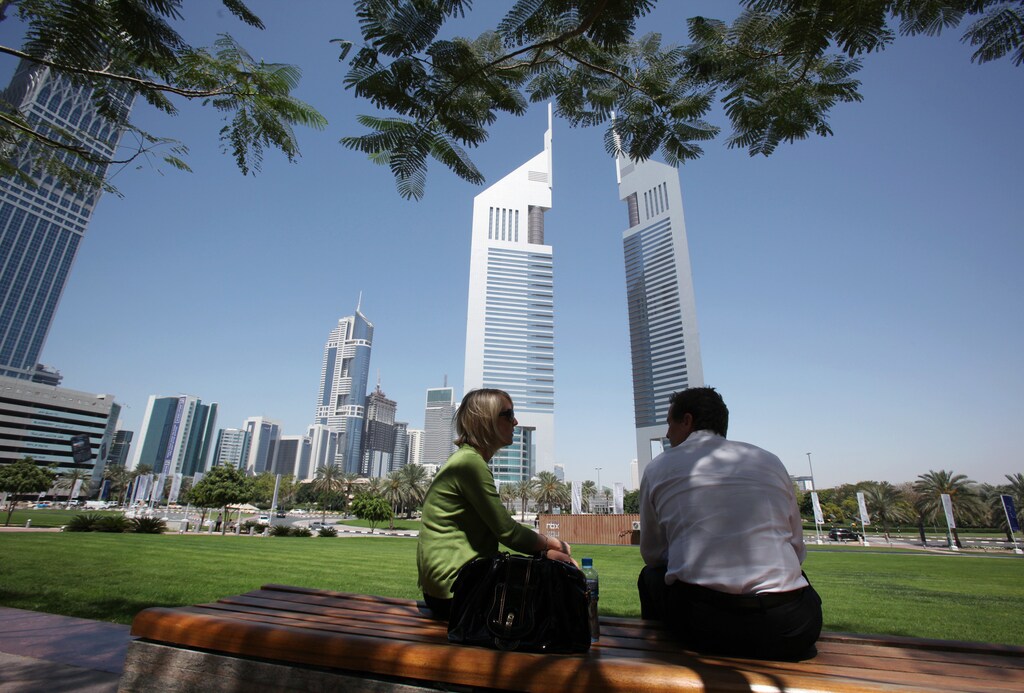People sit on a bench in front of the Emirates Towers at the Dubai International Financial Centre March 21, 2010.