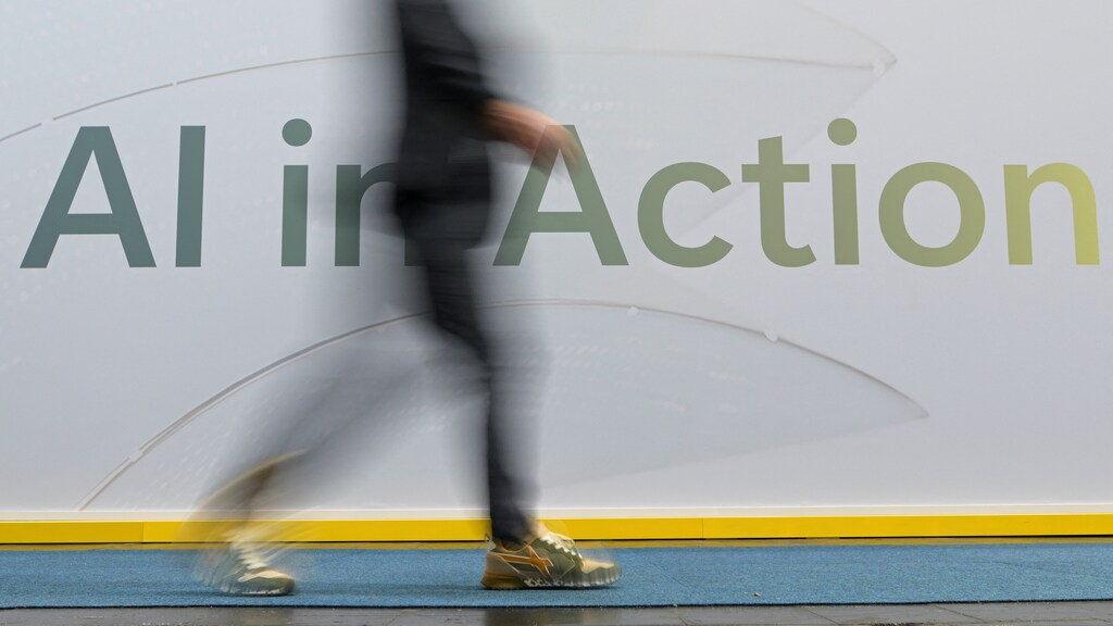 Una persona pasa junto a una inscripción que dice «AI in Action» (IA en acción) en Hannover, Alemania, el 31 de marzo de 2025: Los servicios digitales y la IA todavía no se han visto afectados por los nuevos aranceles de EE. UU.