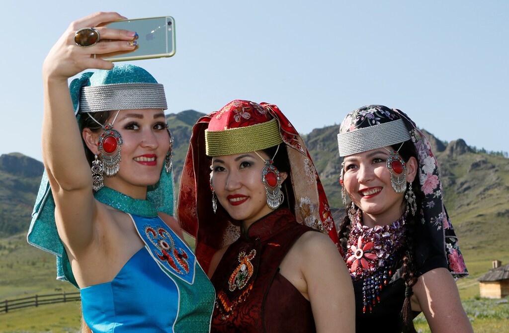 Models of the "Altyr" fashion theatre, dressed in Khakas national costumes, take a selfie during a break in a photo session, as a part of the rehearsal for the Tun-Pairam traditional holiday (The Holiday of the First Milk) celebration at a museum preserve outside Kazanovka village near Abakan in the Republic of Khakassia, Russia, May 28, 2016. The "Khakas aal" (Khakas settlement) ethnographic complex demonstrates the model of a traditional local settlement of the 19th century based on local traditional wooden yurts. The museum preserve is located in a picturesque forest-steppe valley near the Abakan ridge of the Kuznetsk Alatau mountain range and displays numerous objects of the cultural and historical heritage of various epochs accumulated by the people living on this territory, according to representatives. REUTERS/Ilya Naymushin - D1BETGZSWUAB