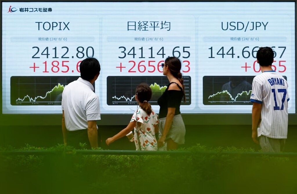 Passersby look at an electronic board displaying Topix, Japan's Nikkei share averages, and Japanese yen exchange rate against the U.S. dollar. Caption: Carry trades played a significant role in the collapse of the Japanese stock market.