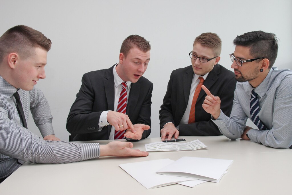 4 men sat at a desk discussing.