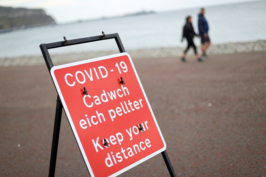 A social distancing sign is seen as people walk in the background, as the Welsh Government is set to impose stricter lockdown measures to try to curb the spread of the coronavirus disease (COVID-19), in Llandudno, Britain October 19, 2020. REUTERS/Carl Recine - RC2OLJ9T9107
