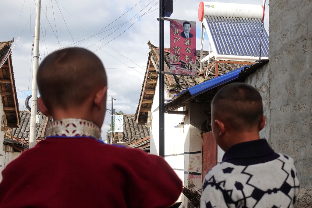 Yi ethnic minority boys stand in front of a board showing Chinese President Xi Jinping on a street in Butuo County, Sichuan province, China July 20, 2017. Picture taken July 20, 2017. REUTERS/Natalie Thomas - RC1783B1EFC0
