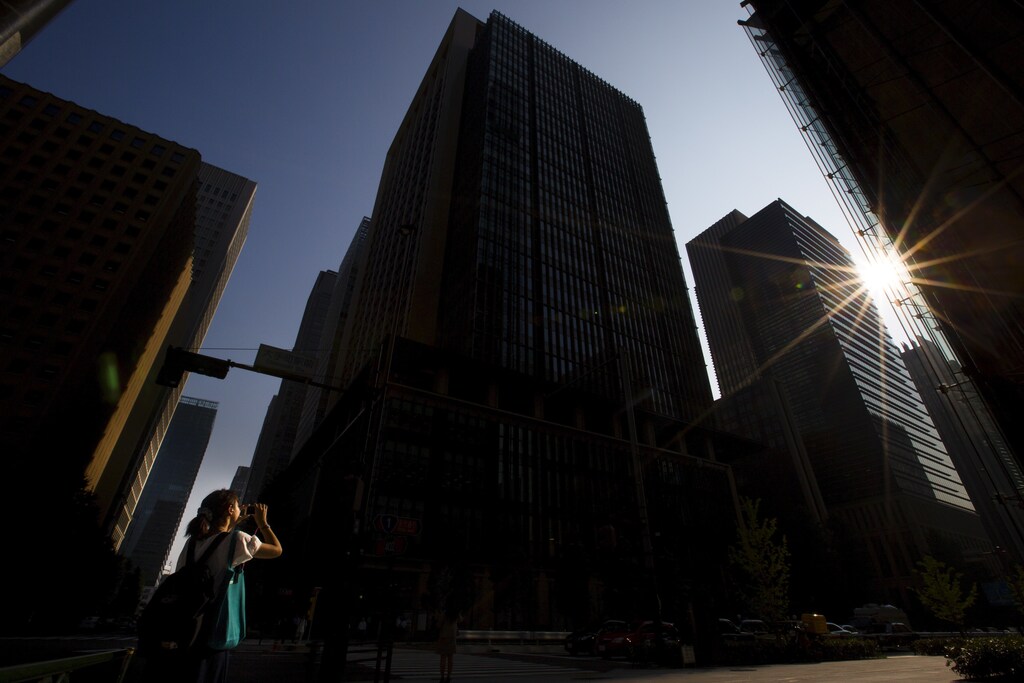 A woman takes pictures as the sun breaks through skyscrapers housing Japan's major banks Mitsubishi UFJ Financial Group Inc (MUFG) and Mizuho Financial Group Inc in Tokyo July 31, 2015. Japan's top banks posted on Friday higher first-quarter profits that exceeded expectations as strong domestic equity markets boosted their brokerage businesses and drove gains from stock holdings. REUTERS/Thomas Peter - GF20000009693