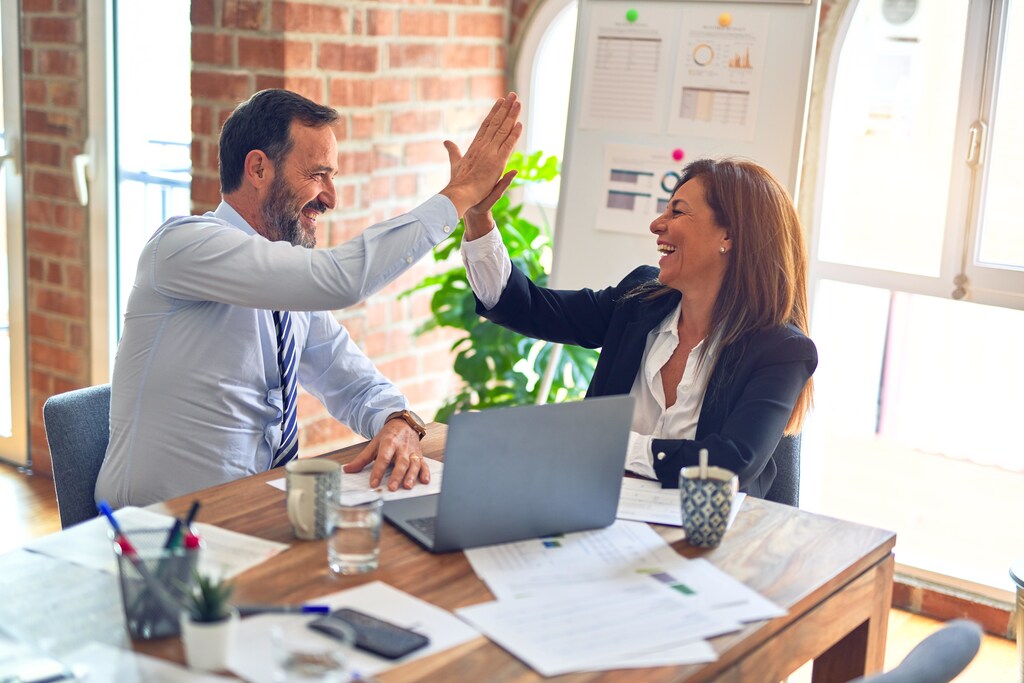 Two business workers working together with smiles, giving high fives at the office.