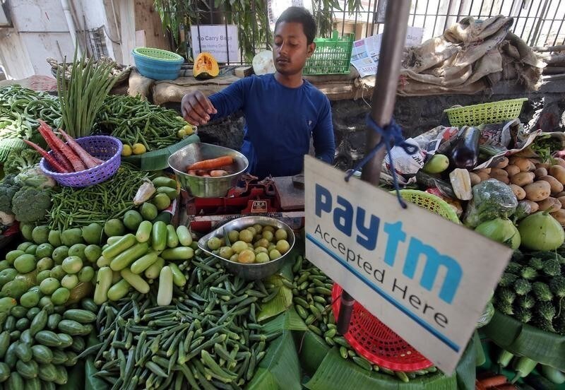 A vendor weighs vegetable next to an advertisement of Paytm, a digital payments firm, hanging amidst his vegetables at a roadside market in Mumbai, India, April 2, 2019. REUTERS/Francis Mascarenhas - RC154FB19320