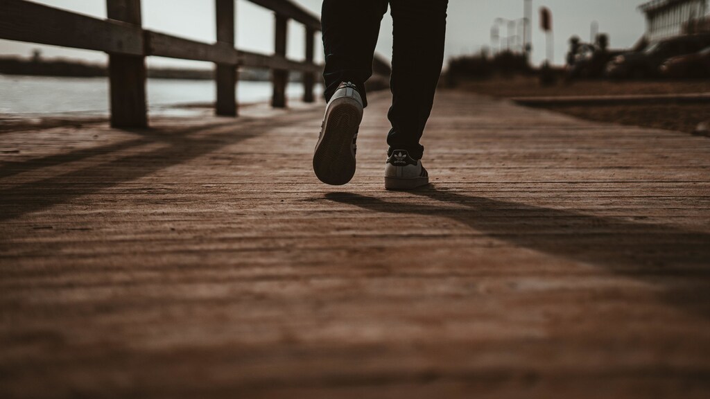 Person walking in white trainers on wooden boardwalk.