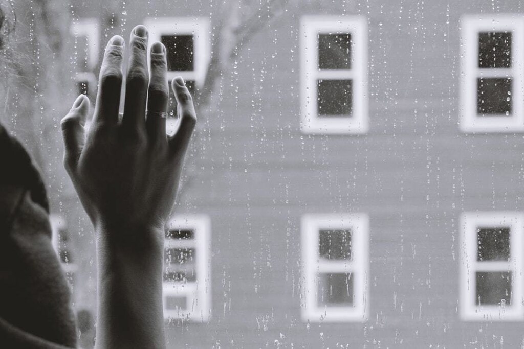 A person rests their hand on the window whilst looking outside.