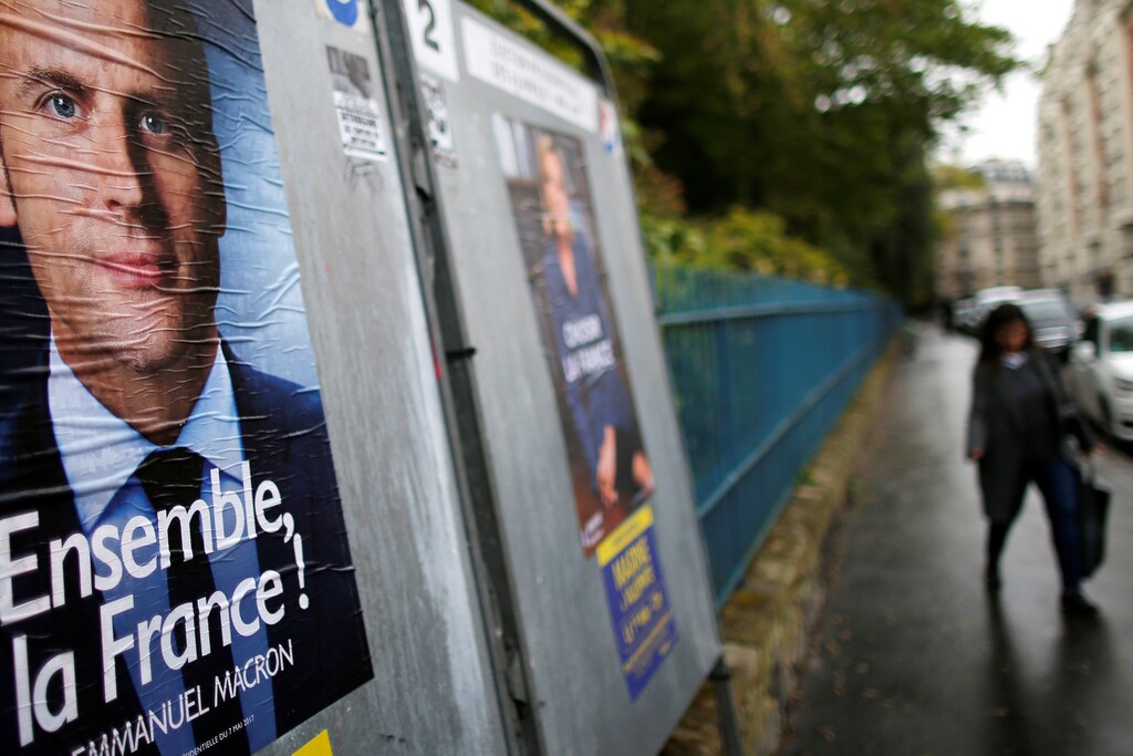 A woman walks past new official posters of candidates for the 2017 French presidential election Emmanuel Macron, head of the political movement En Marche !, or Onwards !, (L) and Marine Le Pen, French National Front (FN) political party leader (R), in Paris, France, April 28, 2017. REUTERS/Gonzalo Fuentes - RTS14DP9