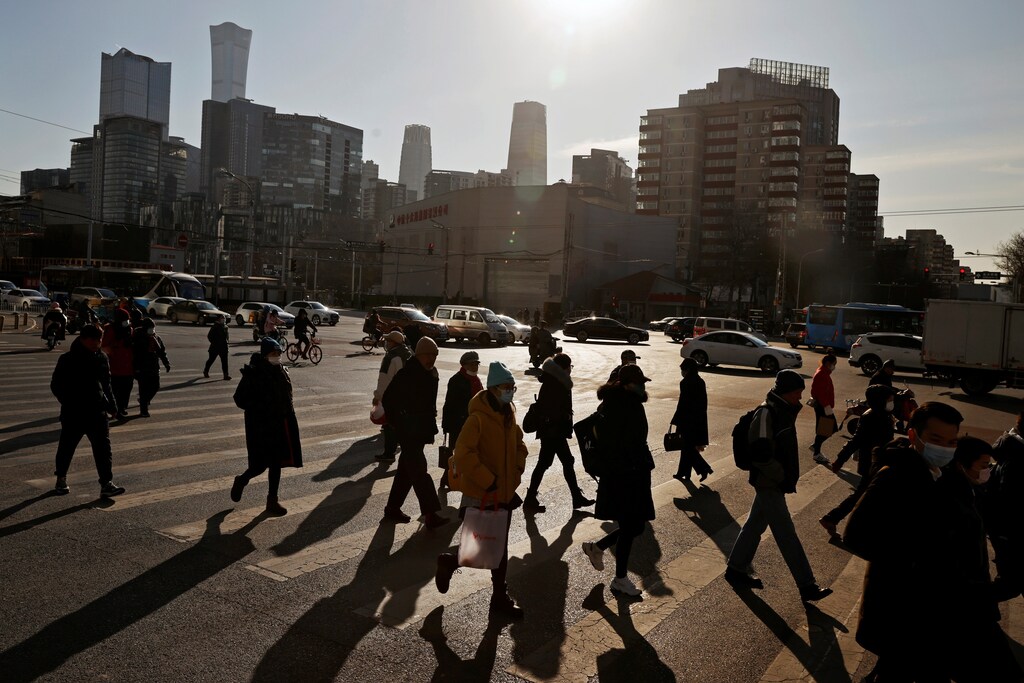 People cross a street during morning rush hour in front of the skyline of the central business district in Beijing, China.