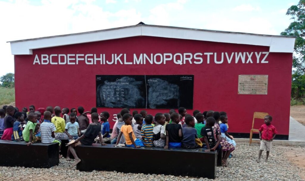 students are seen sitting on benches outside the newly opened 3D-printed school, which was built in 15 hours, in Salima, Malawi