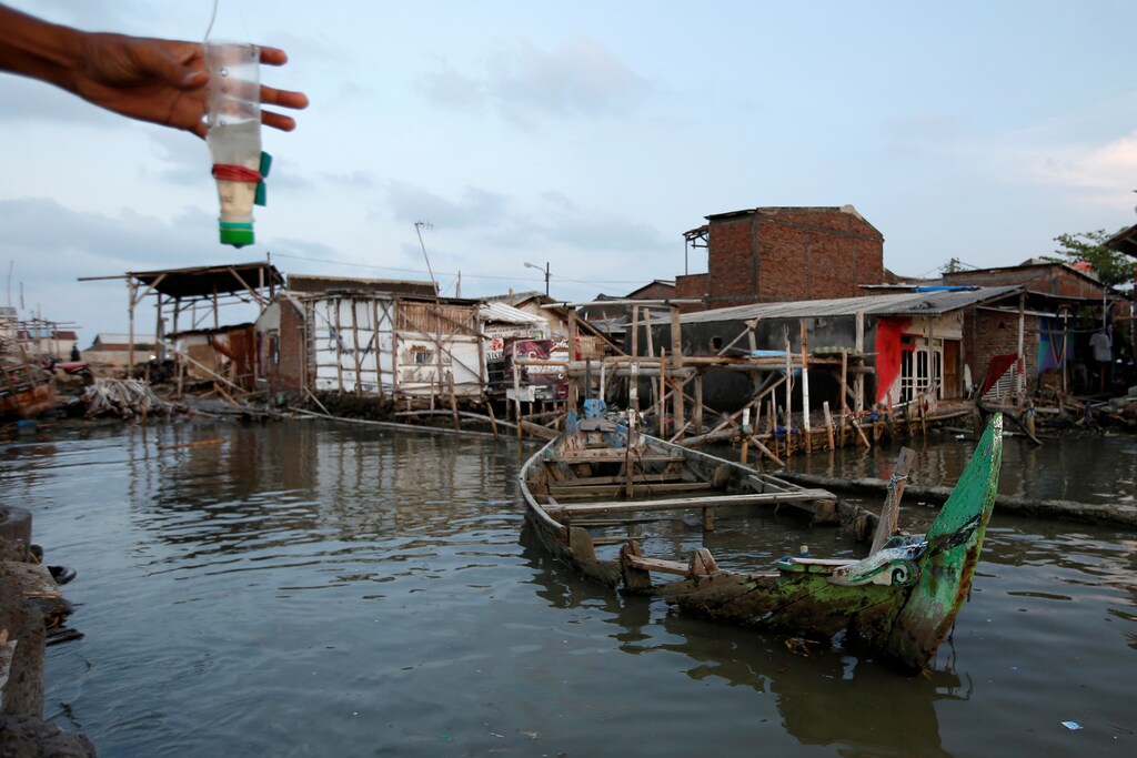 A damaged wooden boat is pictured as a man fishes at Tambaklorok village, which has been affected by rising sea level and land subsidence, in Semarang, Central Java province, Indonesia, November 26, 2019. Picture taken November 26, 2019. REUTERS/Willy Kurniawan - RC22MD9OKEEF