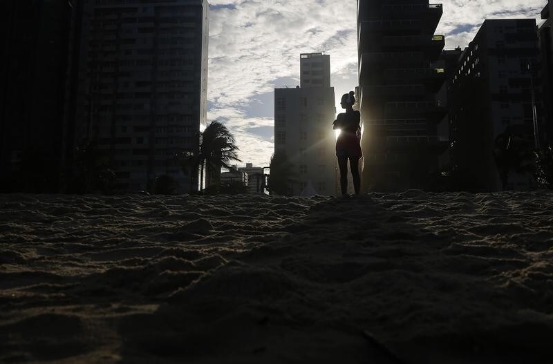 A woman listens to music as the sun sets as seen between buildings on Boa Viagem beach in Recife June 30, 2014. In a project called "On the Sidelines" Reuters photographers share pictures showing their own quirky and creative view of the 2014 World Cup in Brazil. REUTERS/Brian Snyder (BRAZIL - Tags: SPORT SOCCER WORLD CUP TRAVEL ENVIRONMENT SOCIETY) - GM1EA710EOX01