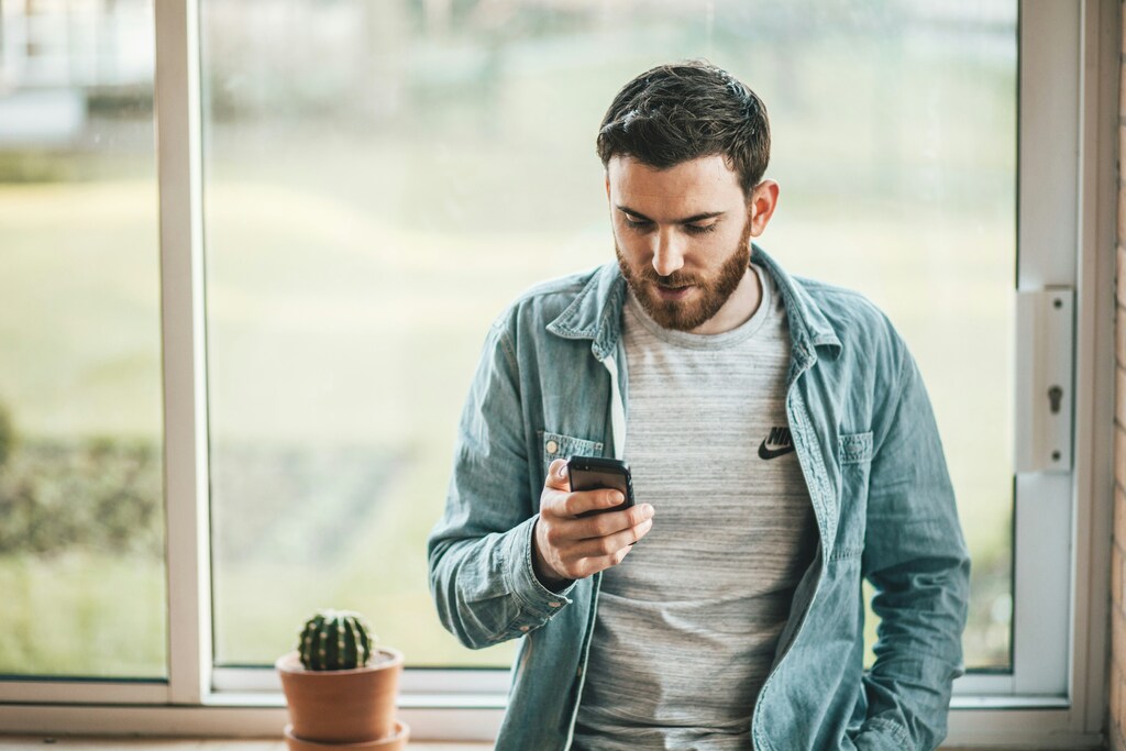 Man in blue shirt by window looking worriedly at his phone: The first step to mitigating GenAI threats is education.