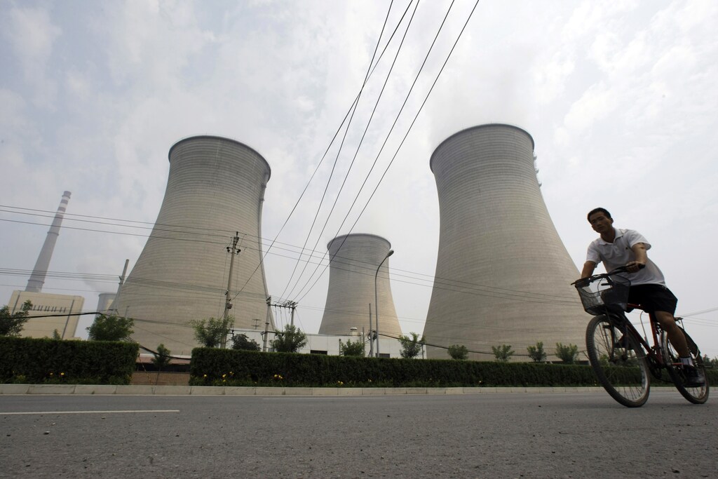 A man rides a bicycle past water cooling towers at a coal-fired power plant in Beijing, 21 July 2008.