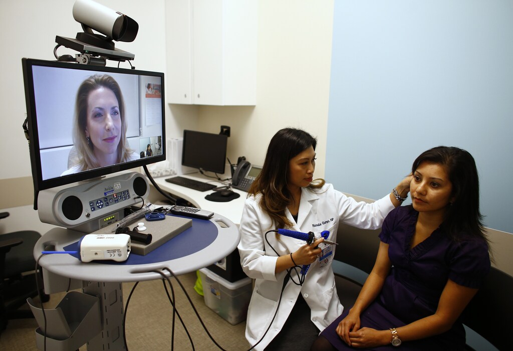 Nurse Health Practitioner Rachelle Quimpo (C) begins an ear exam on patient Shreya Sasaki as Dr. Heidi Meyer remotely views the procedure on a video screen at a newly opened Kaiser Permanente health clinic inside a Target retail department store in San Diego, California November 17, 2014. Four clinics are scheduled to open in Southern California to provide pediatric and adolescent care, well-woman care, family planning, and management of chronic conditions like diabetes and high blood pressure for Kaiser members and non-members. REUTERS/Mike Blake (UNITED STATES - Tags: HEALTH BUSINESS) - RTR4EHX1