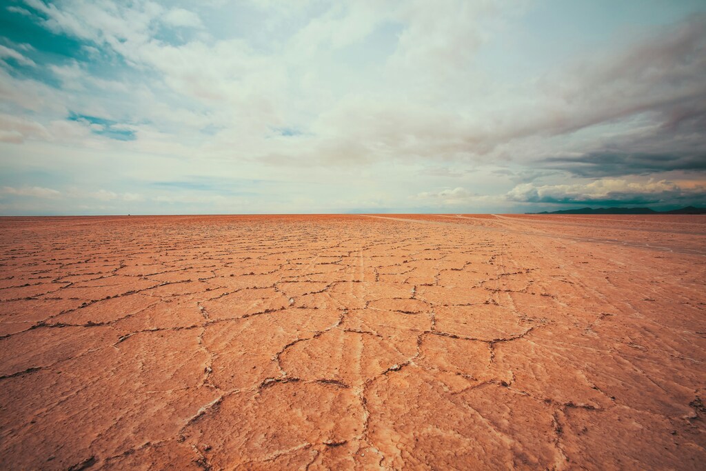 Desierto árido y tierra agrietada bajo un cielo azul con nubes blancas.