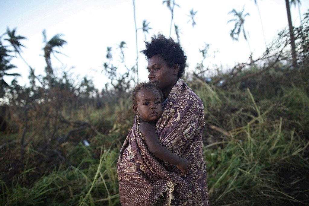A woman carrying her baby walks past fallen trees in Tanna March 18, 2015. International aid agencies ramped up appeals for cyclone-hit Vanuatu on Wednesday, warning that the powerful storm which affected more than two-thirds of the South Pacific island nation had wiped out crops and destroyed fishing fleets, raising the risk of hunger and disease. Residents of the southern island of Tanna said food and basic supplies were running low while relief workers were still battling to reach many islands pummelled by Cyclone Pam's gusts of more than 300 kph (185 mph) on Friday and Saturday. REUTERS/Edgar Su (VANUATU - Tags: ENVIRONMENT DISASTER) - RTR4TRS4