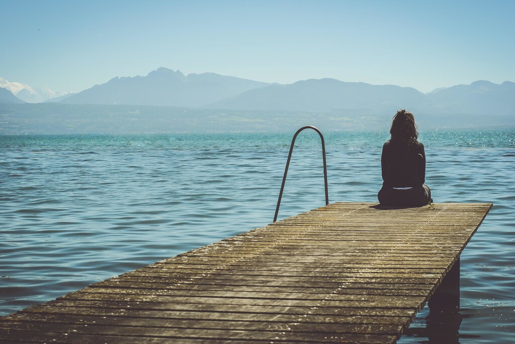 A woman sitting at a dock, looking at the water.
