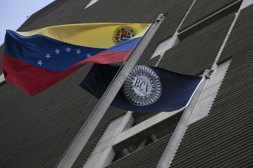 Flags of Venezuela (L) and the Central Bank are seen at the central bank building in Caracas February 10, 2015. Venezuela on Tuesday launched a new foreign exchange platform that will likely devalue the bolivar heavily in efforts to bolster state coffers amid tumbling oil revenue, but risks a spike in already soaring inflation. REUTERS/Jorge Silva (VENEZUELA - Tags: POLITICS BUSINESS) - RTR4P1ZW