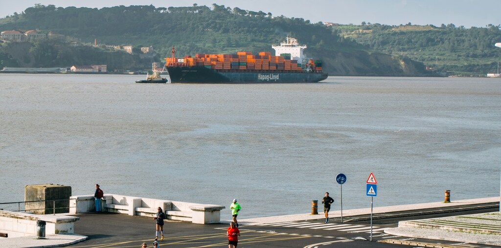 Cargo ships sails on a wide river near a town with people running in sight: The trade financing gap is rising despite underlying trade being stable