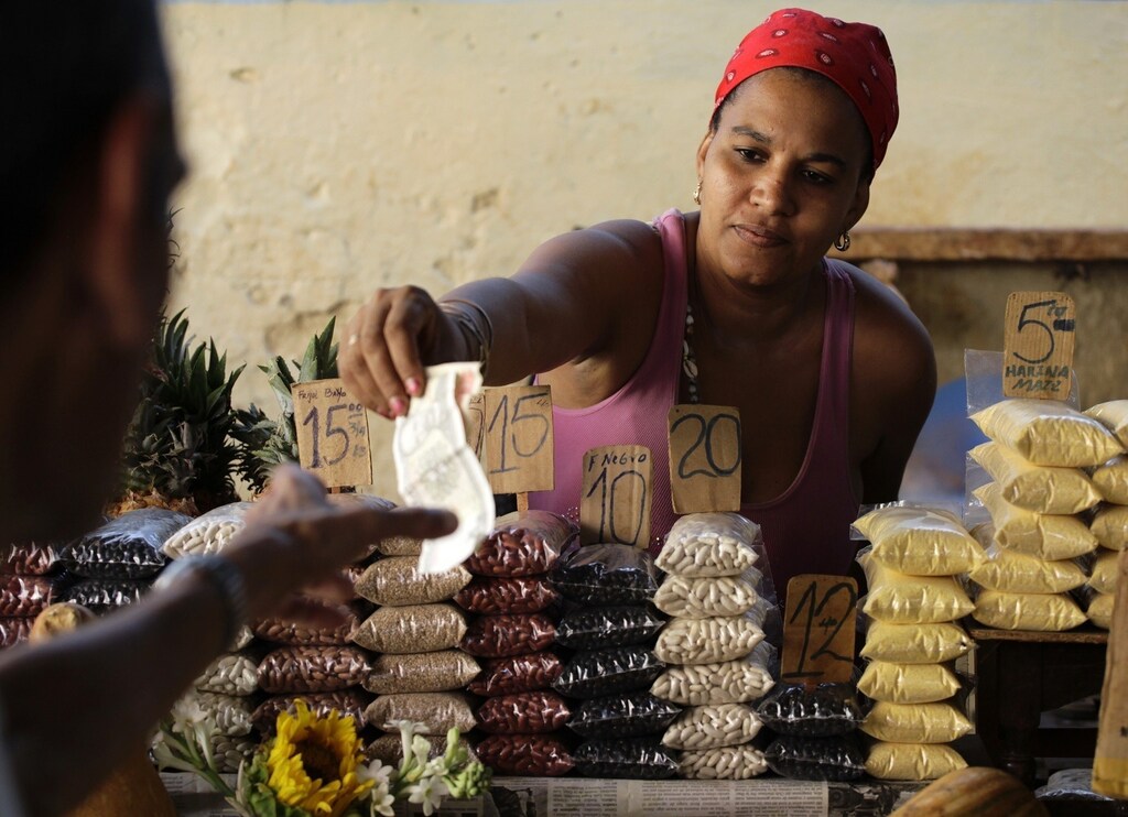 A vendor hands change back to a customer at her market stall with price tags marked in Cuban pesos in Havana October 23, 2013. Cuba took the first step towards scrapping its two-tier currency on October 22, 2013, in a move which could boost local workers' income and remove a major hurdle for importers and exporters. Cuba's convertible peso (CUC) is pegged to the U.S. dollar, while the local peso (CUP) is valued at a fraction of the greenback's value, angering the population which is paid in the latter, and complicating accounting, the evaluation of performance, and trade for state companies.