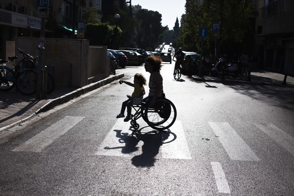 Pascale Bercovitch carries her daughter Mica, 3, on her wheelchair as they cross a road near their home in Tel Aviv May 16, 2012. Bercovitch, 44, who lost her legs in a train accident in France in 1984, will represent Israel at the London Paralympics in hand cycling events. Picture taken May 16, 2012. REUTERS/Nir Elias (ISRAEL - Tags: SPORT OLYMPICS SOCIETY) - RTR34SPK
