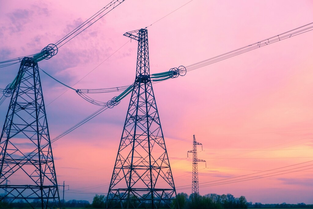 Electricity transmission towers silhouetted against a vibrant sunset sky.